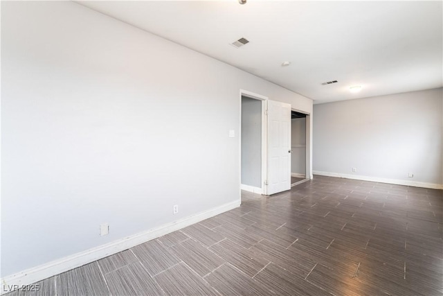 empty room with dark wood-type flooring, visible vents, and baseboards