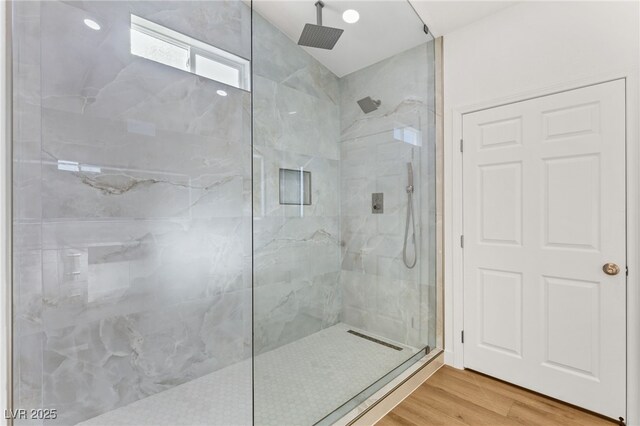 bathroom with a marble finish shower and wood finished floors
