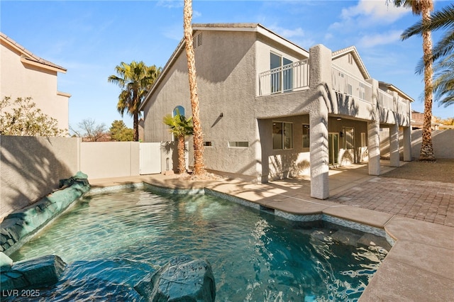 back of house with a fenced backyard, stucco siding, a patio, a balcony, and a fenced in pool