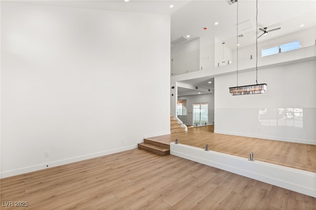 unfurnished living room with a towering ceiling, baseboards, recessed lighting, light wood-style floors, and visible vents