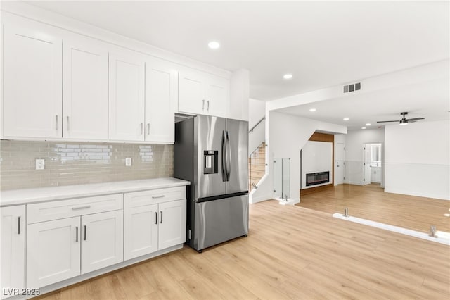 kitchen with white cabinets, stainless steel refrigerator with ice dispenser, light countertops, light wood finished floors, and decorative backsplash