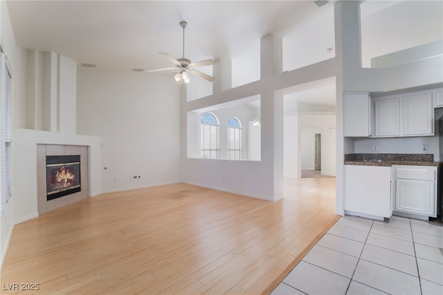 4176 Skywalker Ave, Las Vegas, NV 89120 - unfurnished living room featuring light wood-style floors, a ceiling fan, a tiled fireplace, a towering ceiling, and baseboards