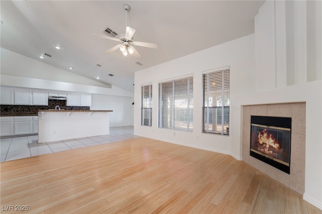 4176 Skywalker Ave, Las Vegas, NV 89120 - unfurnished living room featuring light wood-style floors, vaulted ceiling, ceiling fan, a tile fireplace, and a sink