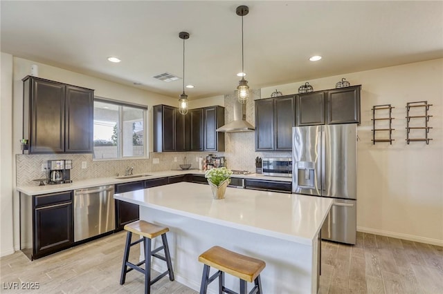 7445 Tinley Creek Ave, Las Vegas, NV 89113 - kitchen with wall chimney exhaust hood, tasteful backsplash, stainless steel appliances, light wood finished floors, and a breakfast bar area