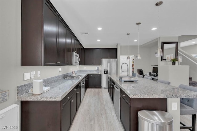 301 Resolute Ave, Henderson, NV 89011 - kitchen with stainless steel appliances, light wood-style flooring, a breakfast bar, dark brown cabinetry, and a large island with sink