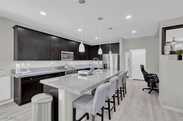 301 Resolute Ave, Henderson, NV 89011 - kitchen featuring appliances with stainless steel finishes, light wood finished floors, a kitchen bar, a kitchen island with sink, and light stone counters