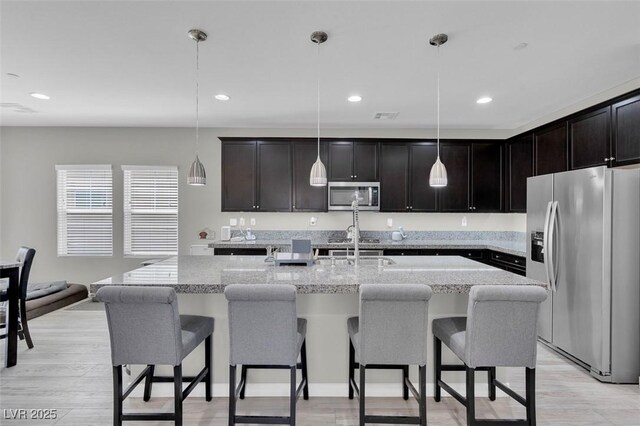 301 Resolute Ave, Henderson, NV 89011 - kitchen featuring appliances with stainless steel finishes, a breakfast bar area, a kitchen island with sink, light stone counters, and recessed lighting