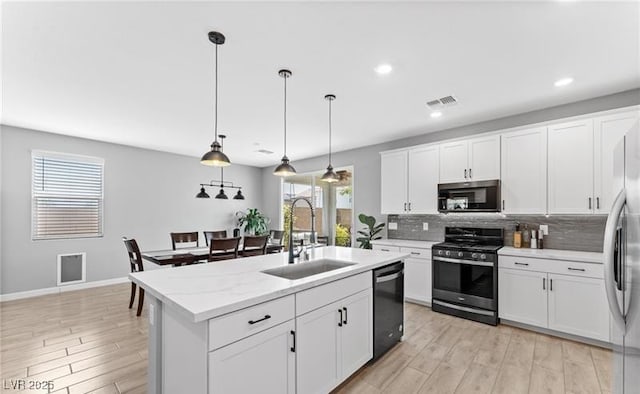 kitchen with a sink, stainless steel appliances, light wood-type flooring, visible vents, and backsplash