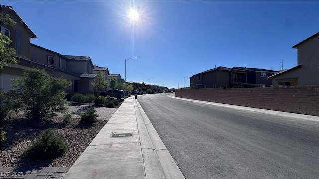 view of asphalt road with a residential view, sidewalks, street lights, and curbs