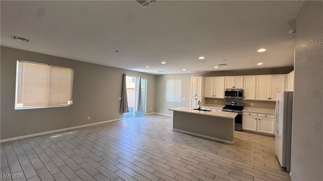 kitchen with appliances with stainless steel finishes, open floor plan, a sink, baseboards, and white cabinetry