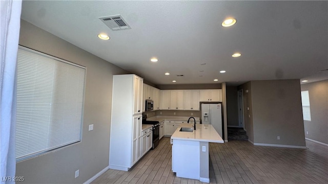 kitchen featuring black gas stove, white fridge with ice dispenser, stainless steel microwave, a sink, and white cabinetry