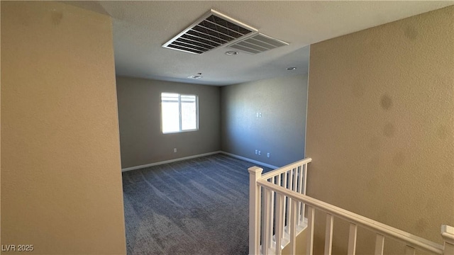 carpeted empty room featuring a textured wall and baseboards