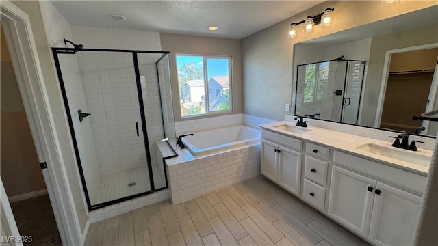 bathroom with a stall shower, a bath, double vanity, wood finished floors, and a walk in closet