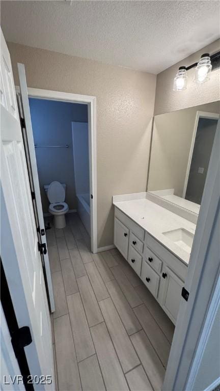 full bathroom with a textured ceiling, vanity, toilet, wood finish floors, and a bathtub