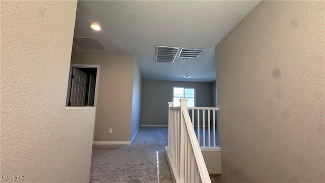 corridor featuring an upstairs landing, carpet floors, a textured wall, and baseboards