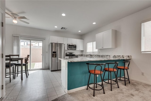 5256 Sherwood Forest Ln, Las Vegas, NV 89122 - kitchen featuring a peninsula, white cabinetry, a ceiling fan, a kitchen bar, and stainless steel appliances