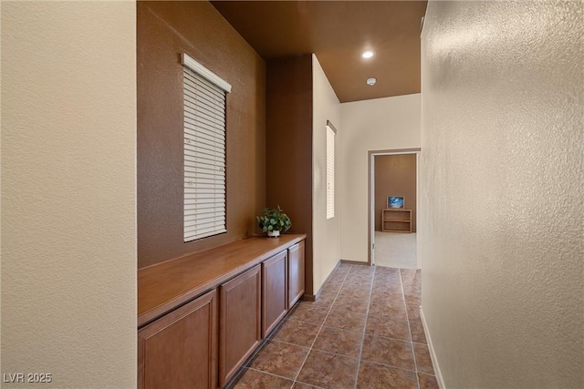 corridor with dark tile patterned floors, recessed lighting, a textured wall, and baseboards