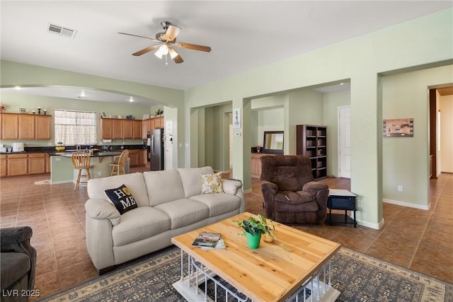living area featuring arched walkways, a ceiling fan, visible vents, tile patterned flooring, and baseboards