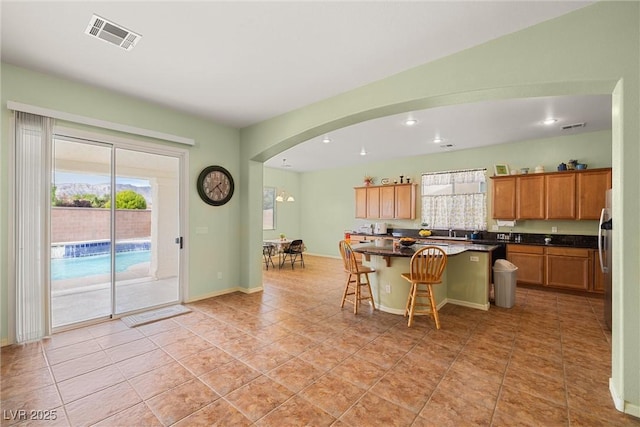 kitchen with dark countertops, visible vents, a breakfast bar area, a healthy amount of sunlight, and arched walkways