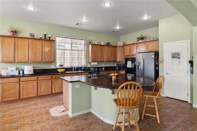 kitchen with a kitchen breakfast bar, brown cabinetry, black appliances, a center island, and a sink