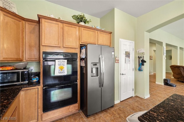 kitchen with brown cabinets, light tile patterned flooring, dark stone counters, and stainless steel appliances