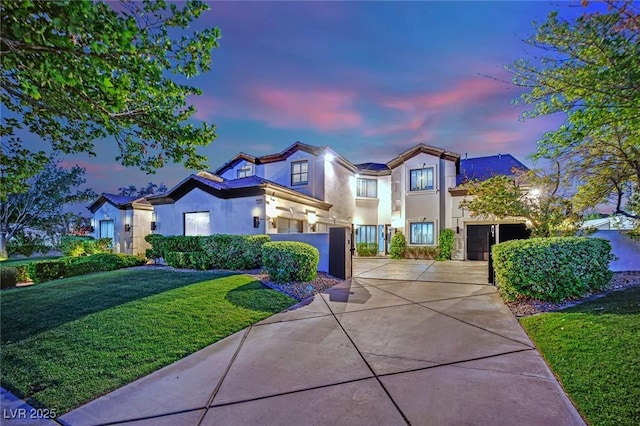 mediterranean / spanish house with a gate, concrete driveway, an attached garage, a yard, and stucco siding