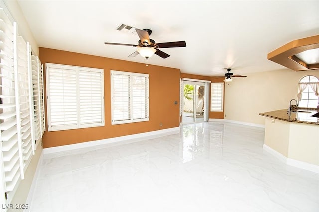 unfurnished living room with a sink, ceiling fan, marble finish floor, and baseboards
