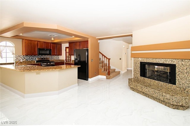 kitchen with a multi sided fireplace, black appliances, marble finish floor, a sink, and a raised ceiling