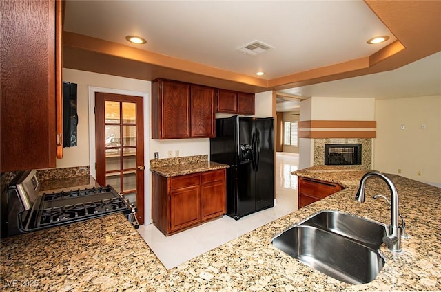 kitchen featuring gas stove, light stone counters, black fridge, visible vents, and a sink