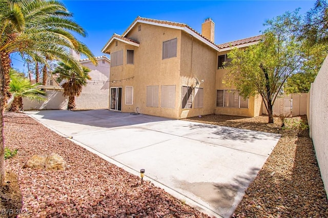 back of house with a fenced backyard, stucco siding, a patio area, a tile roof, and a chimney