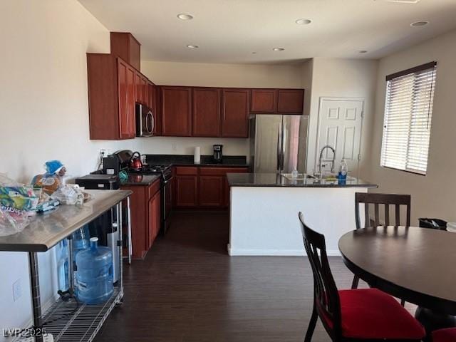 kitchen featuring dark wood-type flooring, dark countertops, a center island with sink, and stainless steel appliances