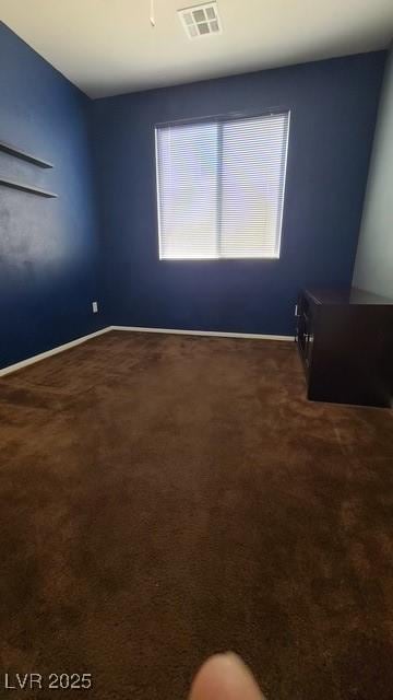 spare room with dark colored carpet, visible vents, and baseboards