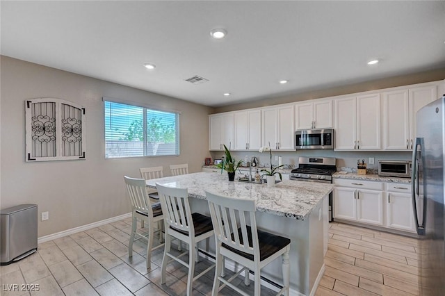 kitchen featuring visible vents, white cabinetry, light stone counters, wood finish floors, and appliances with stainless steel finishes