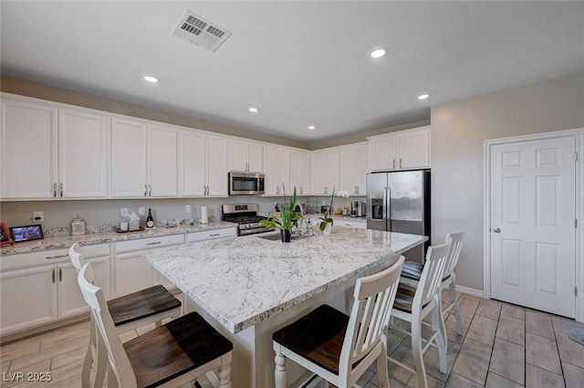 kitchen with a sink, a center island with sink, white cabinets, appliances with stainless steel finishes, and visible vents