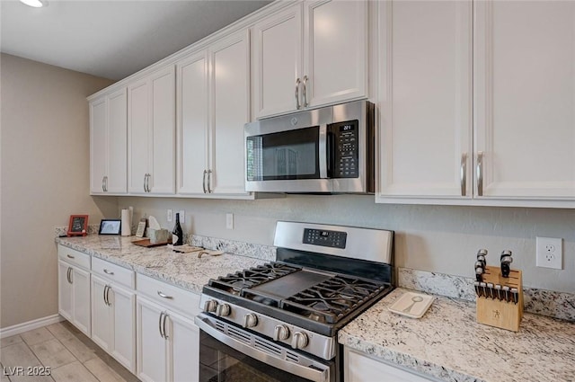 kitchen featuring white cabinets, light stone countertops, appliances with stainless steel finishes, and baseboards