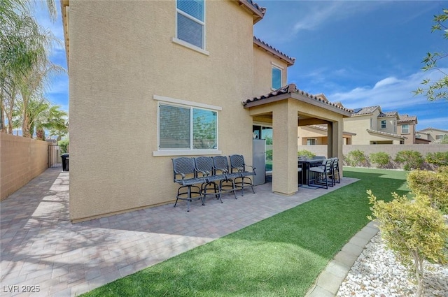 rear view of property with a fenced backyard, stucco siding, a tile roof, a patio area, and a lawn