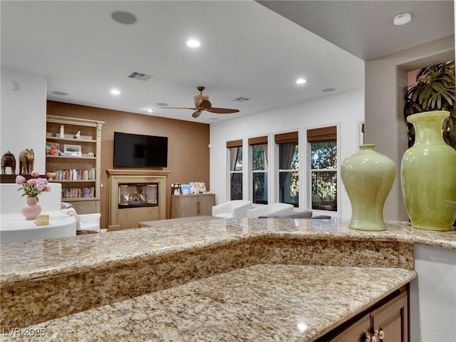 kitchen featuring a glass covered fireplace, visible vents, recessed lighting, ceiling fan, and light stone countertops