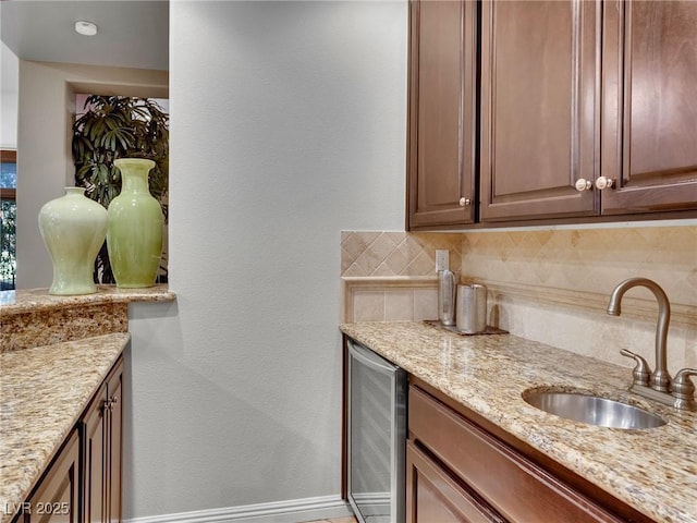 kitchen with a sink, a textured wall, backsplash, light stone countertops, and wine cooler