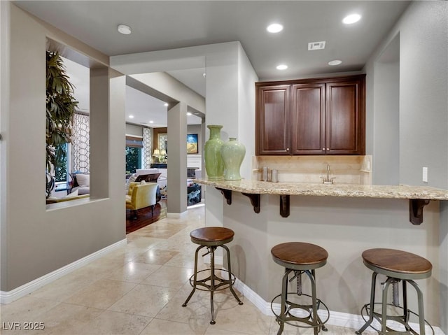 kitchen featuring light stone countertops, decorative backsplash, a breakfast bar, and baseboards