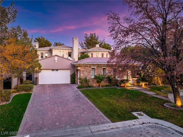 mediterranean / spanish-style house featuring a chimney, stucco siding, driveway, stone siding, and a lawn
