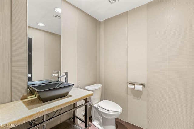 half bathroom with recessed lighting, visible vents, toilet, and a sink