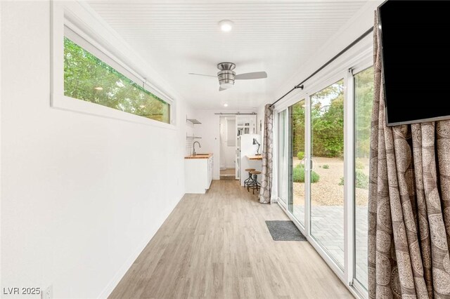 hallway with baseboards, a sink, and light wood-style flooring