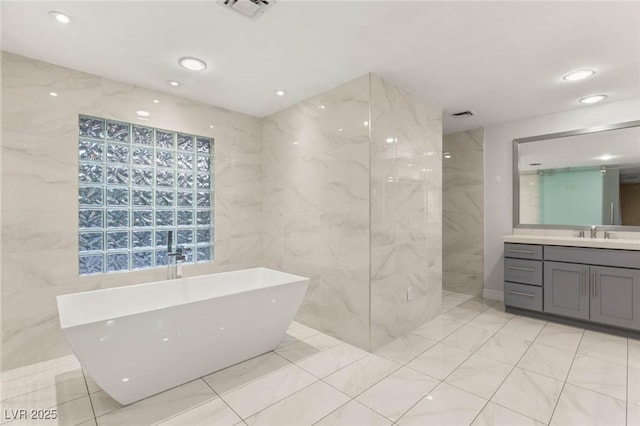 full bath with a freestanding tub, tile walls, visible vents, and vanity