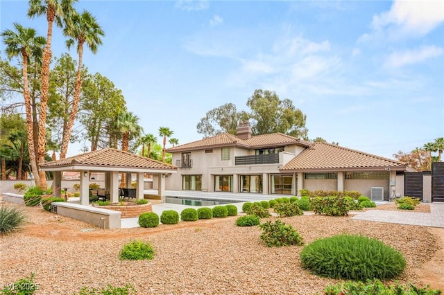 rear view of house featuring a tiled roof, a chimney, a gazebo, and stucco siding