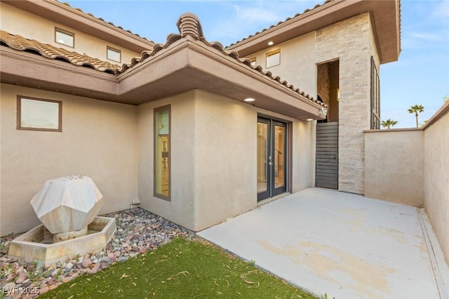 rear view of house with a tile roof, french doors, a patio area, and stucco siding