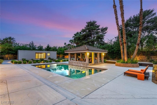 pool at dusk with an outdoor pool, a storage structure, an outbuilding, and a patio
