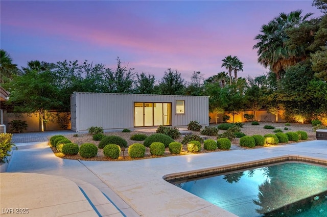 pool at dusk featuring fence, an outdoor pool, and a patio area