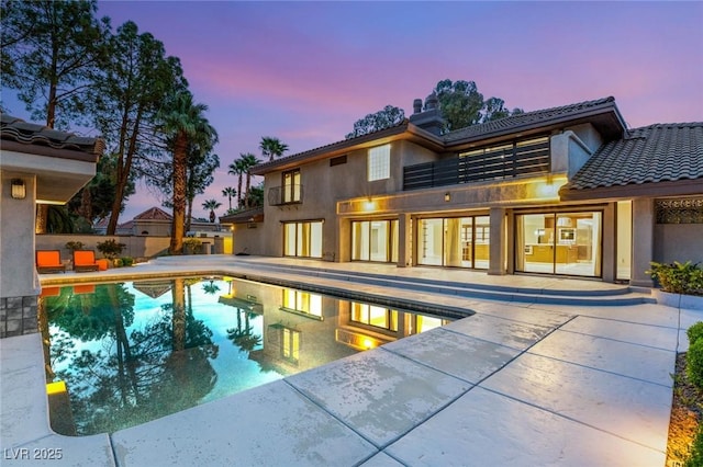 rear view of house with fence, an outdoor pool, a balcony, and a patio