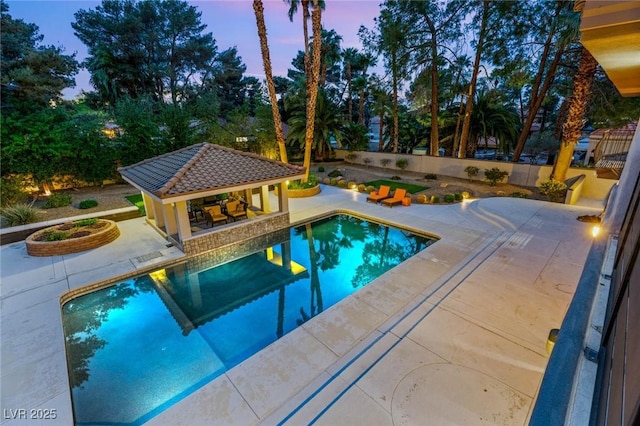 pool at dusk with a patio area, a storage structure, an outdoor pool, an outdoor structure, and fence