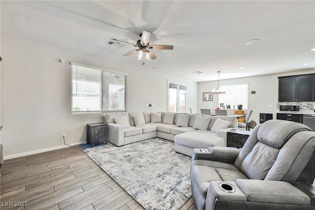 living room with light wood-style floors, ceiling fan with notable chandelier, recessed lighting, baseboards, and visible vents